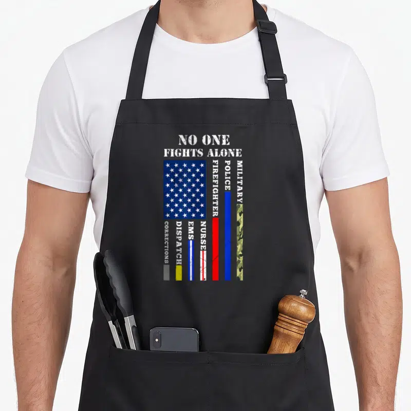 Fight 4th of july apron - No One Fights Alone text above distressed flag and vertical stripes for police, fire — shown on a black cotton canvas apron against a white background