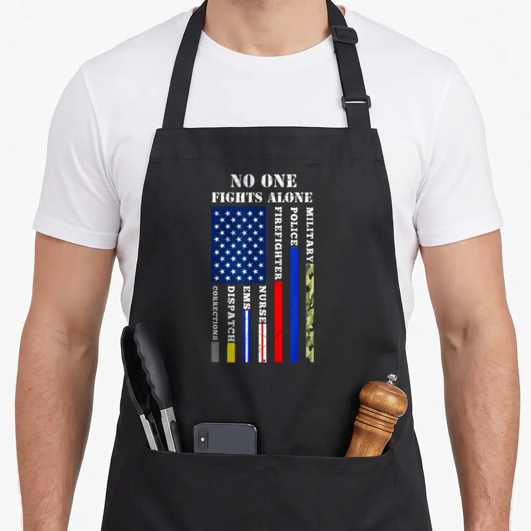 Fight 4th of july apron - No One Fights Alone text above distressed flag and vertical stripes for police, fire — shown on a black cotton canvas apron against a white background