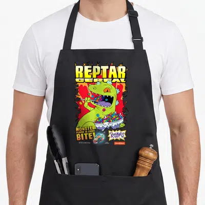 Fruity cereal apron - Reptar eating colorful cereal rings with Monster Flavor text and cartoon logos — shown on a black cotton canvas apron against a white background