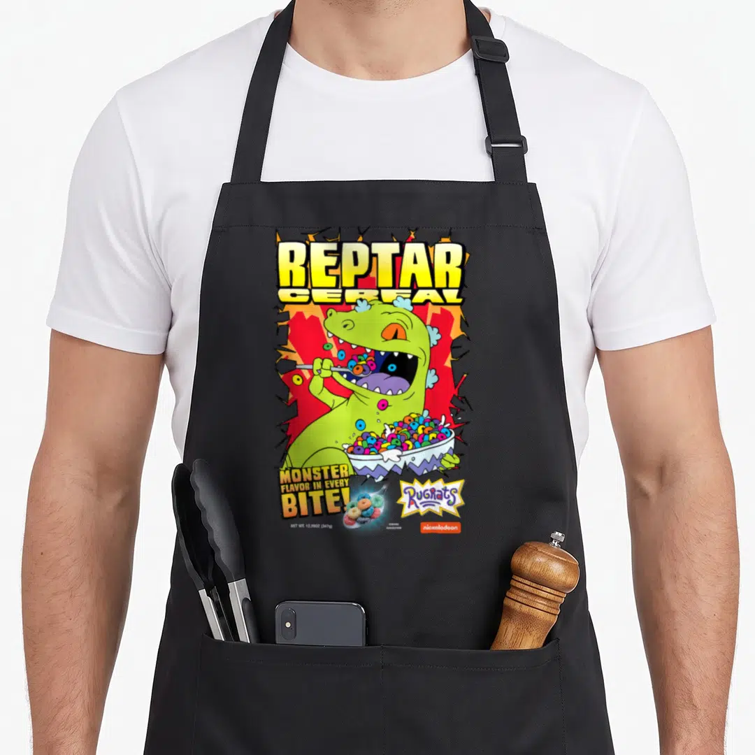 Fruity cereal apron - Reptar eating colorful cereal rings with Monster Flavor text and cartoon logos — shown on a black cotton canvas apron against a white background