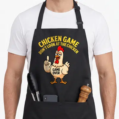 Chicken gag aprons - Cartoon chicken with arched yellow text and GAME OVER written on its chest — shown on a black cotton canvas apron against a white background