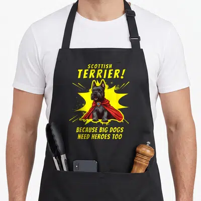 Superdog dog apron - Cartoon Scottish Terrier in red cape with yellow burst and hero text — shown on a black cotton canvas apron against a white background
