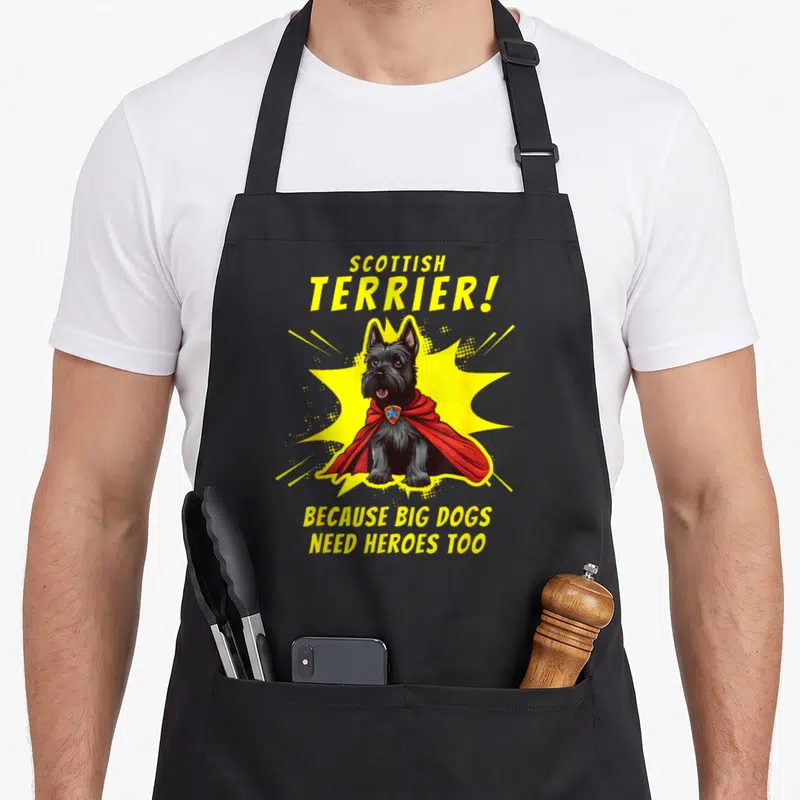 Superdog dog apron - Cartoon Scottish Terrier in red cape with yellow burst and hero text — shown on a black cotton canvas apron against a white background