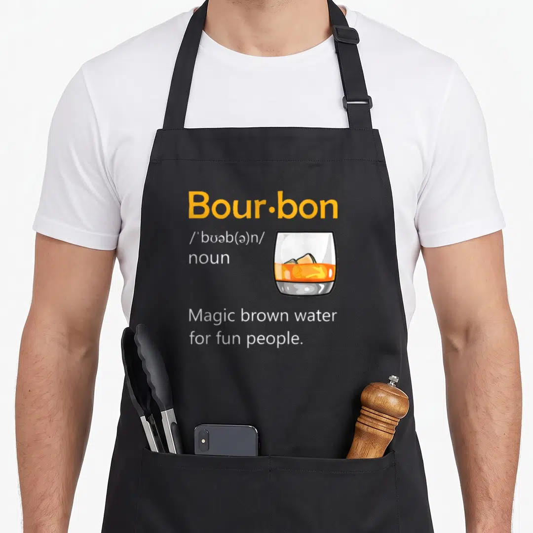 Definition magic apron - Dictionary style text reading Bour·bon and Magic brown water for fun people next to a cartoon — shown on a black cotton canvas apron against a white background