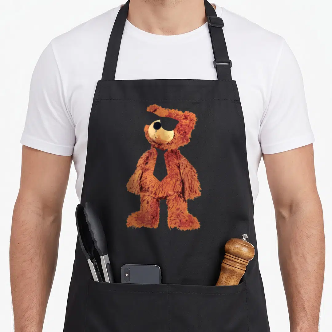 Sunglass teddy bear apron - Fuzzy orange brown teddy bear wearing sunglasses and tie standing upright — shown on a black cotton canvas apron against a white background