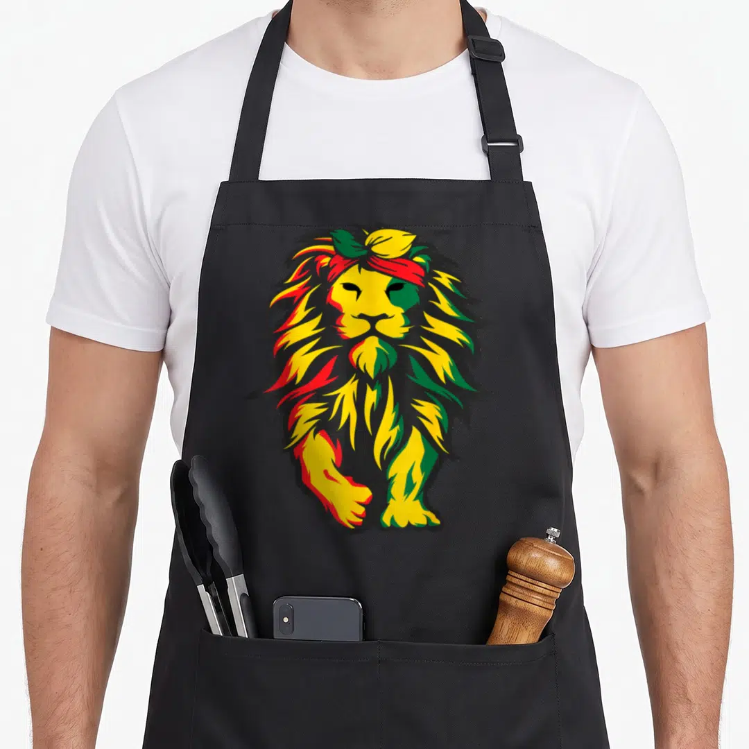 Lion african american aprons - Cartoon lion head in red yellow green and black wearing a headband — shown on a black cotton canvas apron against a white background