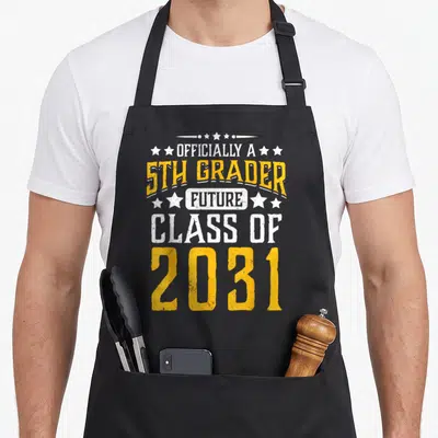 Officially future class apron - White and yellow distressed text reading Officially a 5th Grader Future Class of 2031 — shown on a black cotton canvas apron against a white background