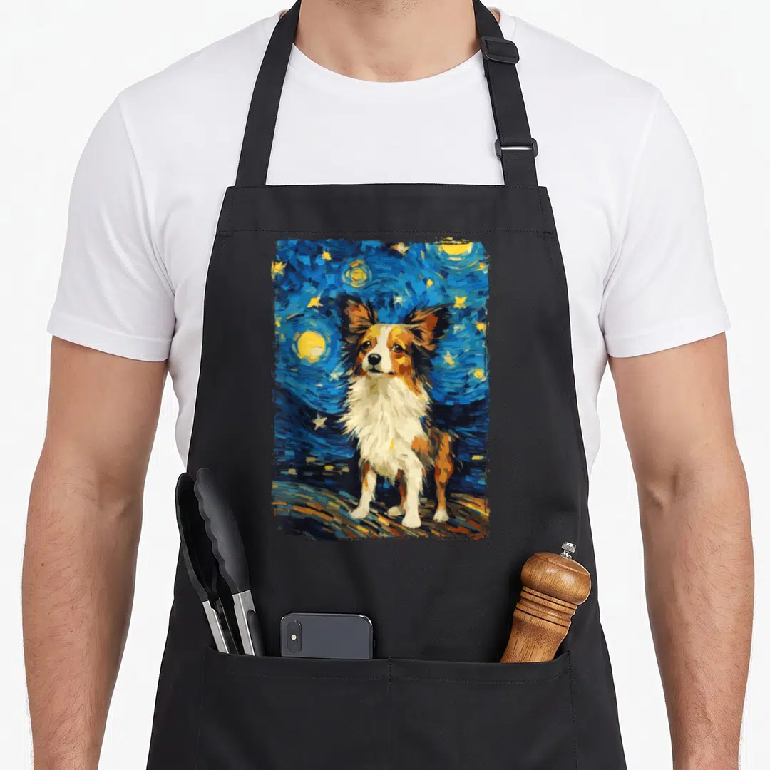 Papillon starry dog apron - Stylized dog portrait against swirling blue night sky with yellow stars and moon — shown on a black cotton canvas apron against a white background
