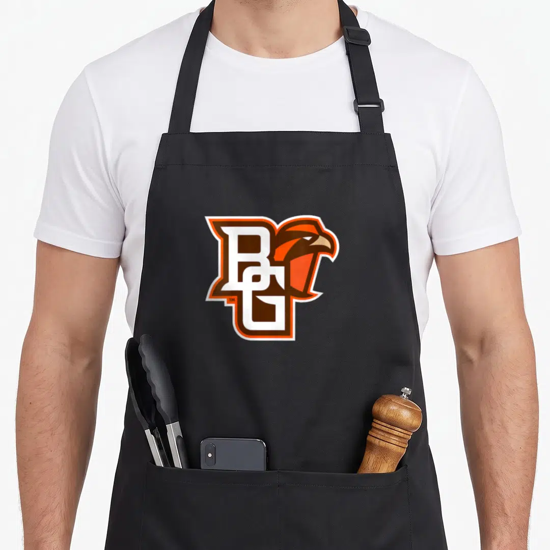 Bowling icon falcon apron - Intertwined BG letters with a falcon head in brown, orange, and white outlines — shown on a black cotton canvas apron against a white background