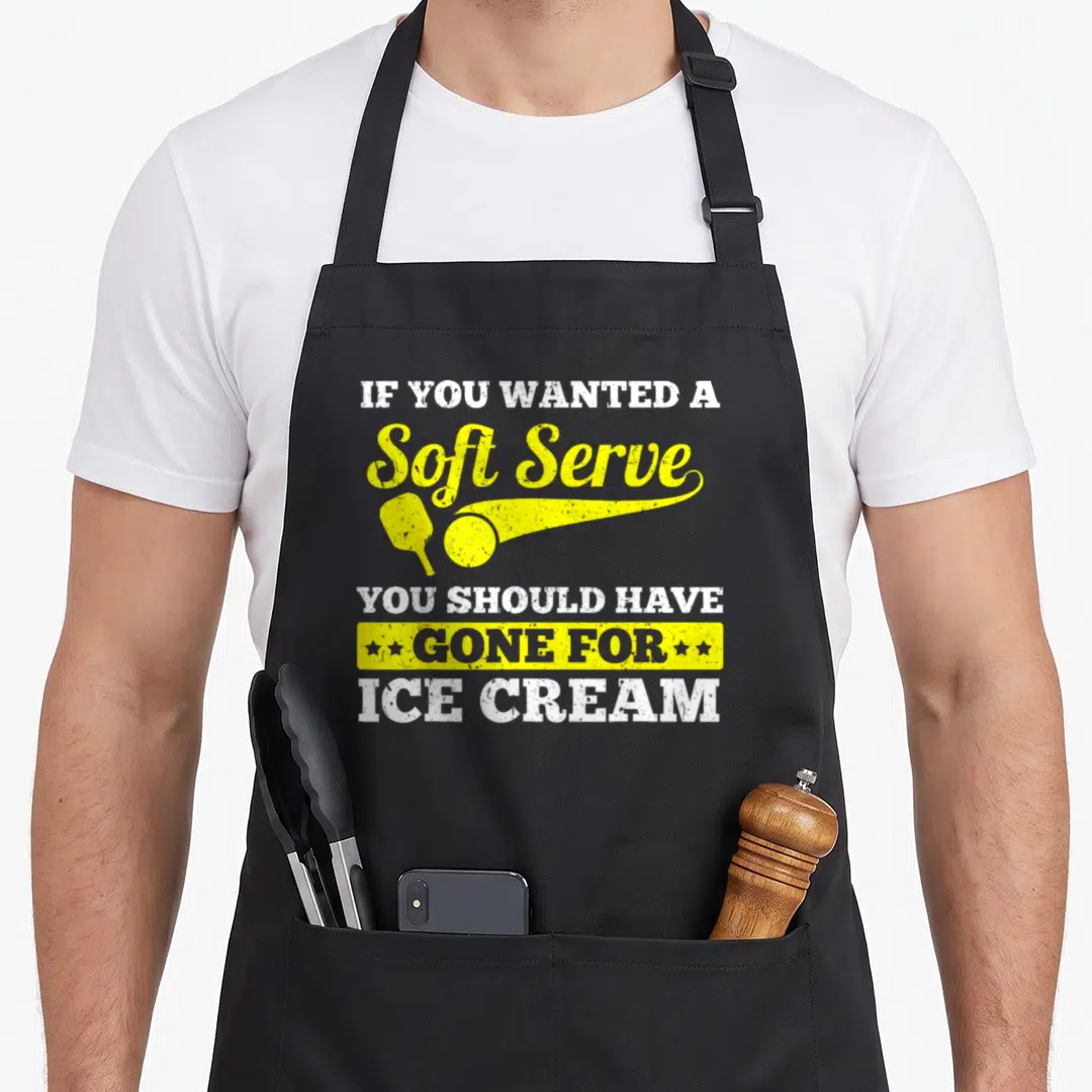 Sport to serve man apron - Pickleball paddle and ball graphic with distressed white and yellow text reading soft serve — shown on a black cotton canvas apron against a white background