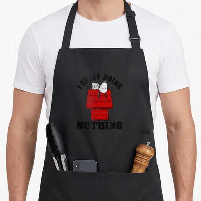 Enjoy peanut addict apron - Snoopy lying on red doghouse with I Enjoy Doing Nothing text — shown on a black cotton canvas apron against a white background