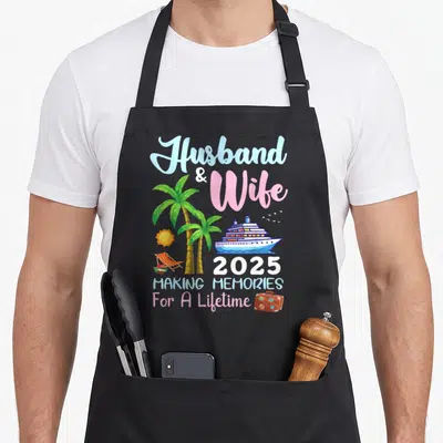 B2shop memory apron - Cartoon cruise ship with palm trees, suitcase, and text Husband Wife 2025 Making Memories — shown on a black cotton canvas apron against a white background