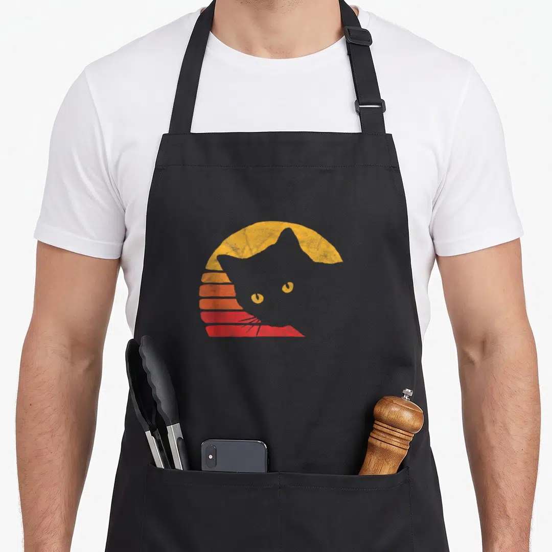 Eighty cat apron - Grey cat silhouette overlaid on yellow orange and red retro striped sun arc — shown on a black cotton canvas apron against a white background