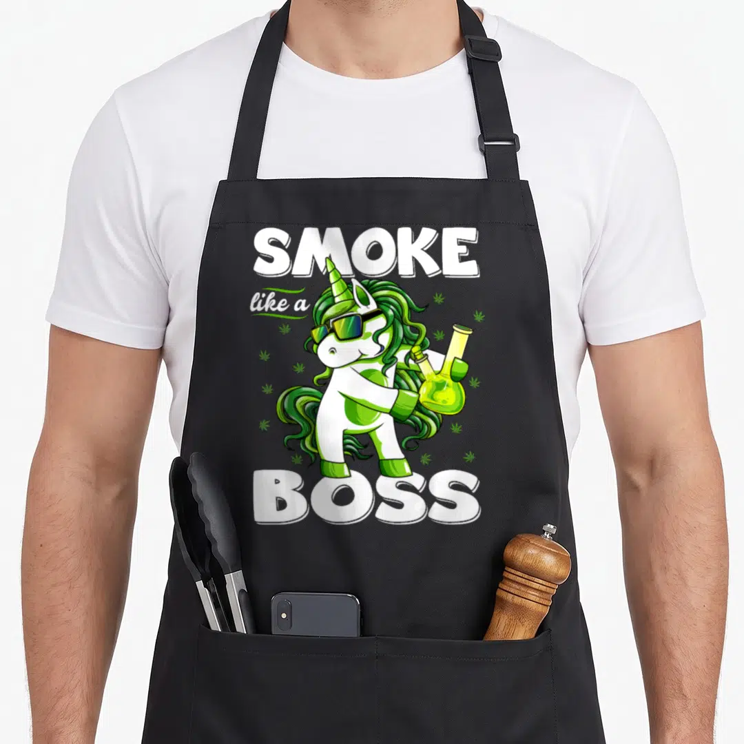 Floss unicorn apron - Cartoon unicorn with green mane holding bong, SMOKE like a BOSS text, cannabis leaves — shown on a black cotton canvas apron against a white background