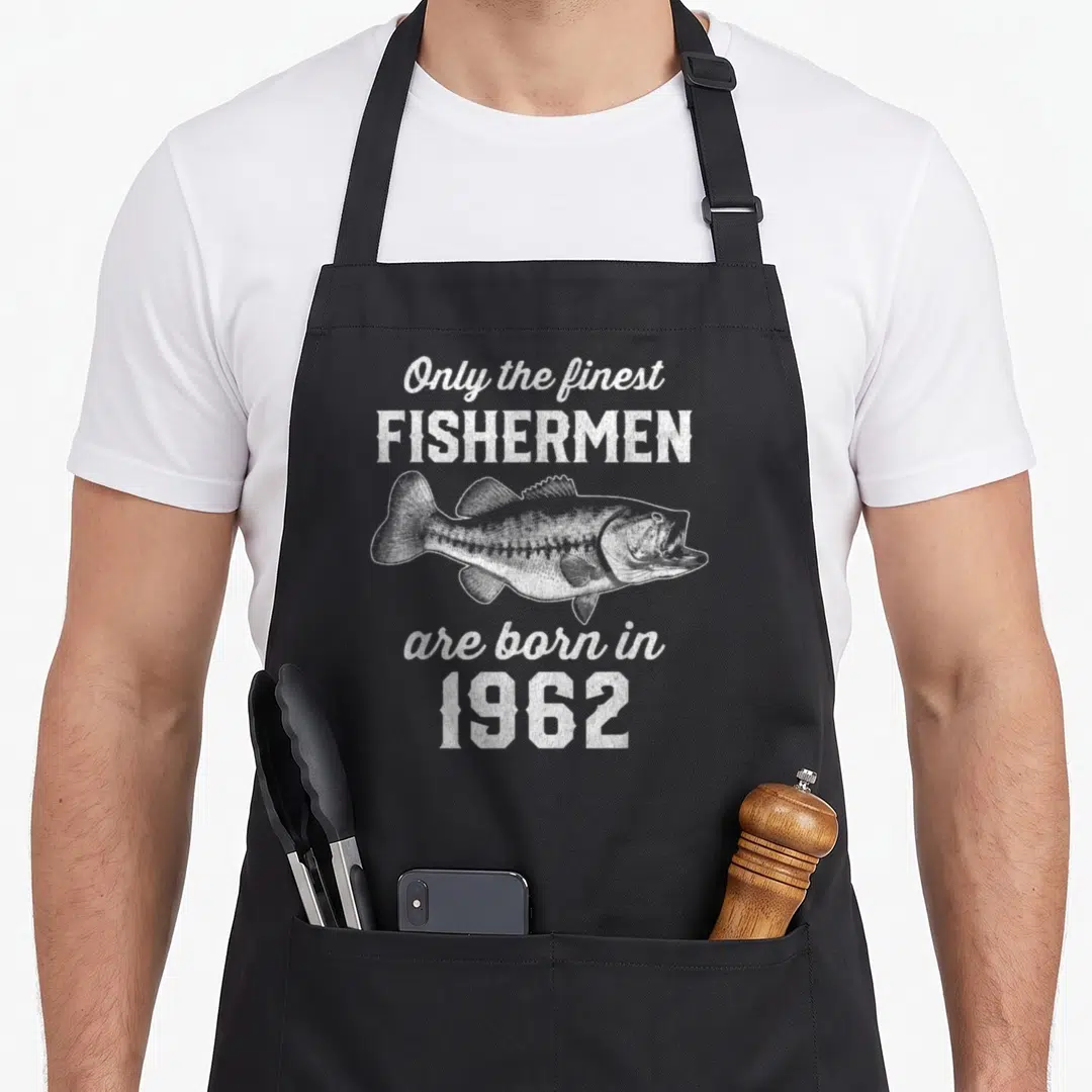 64th fishing aprons - White distressed fish and 1962 text on black bib apron — shown on a black cotton canvas apron against a white background