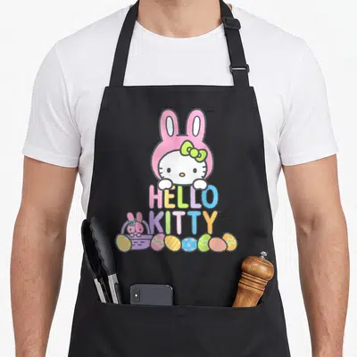 Bunny easter apron - Hello Kitty in pink hood with colorful text and Easter eggs — shown on a black cotton canvas apron against a white background