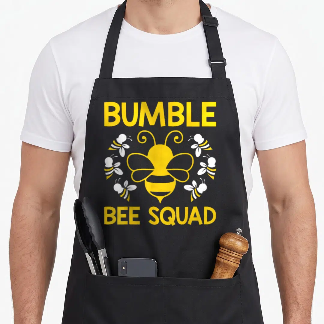Bumble friends cooking apron - Yellow BUMBLE BEE SQUAD text with one large and five small cartoon bees — shown on a black cotton canvas apron against a white background