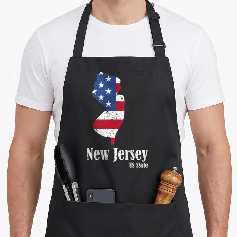 Jersey 4th of july apron - New Jersey state map shape filled with red white and blue stars stripes distressed text below — shown on a black cotton canvas apron against a white background