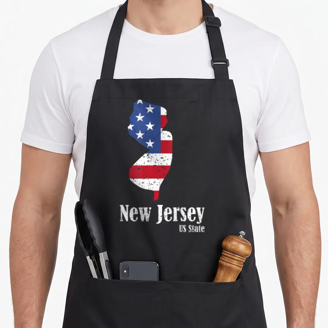 Jersey 4th of july apron - New Jersey state map shape filled with red white and blue stars stripes distressed text below — shown on a black cotton canvas apron against a white background