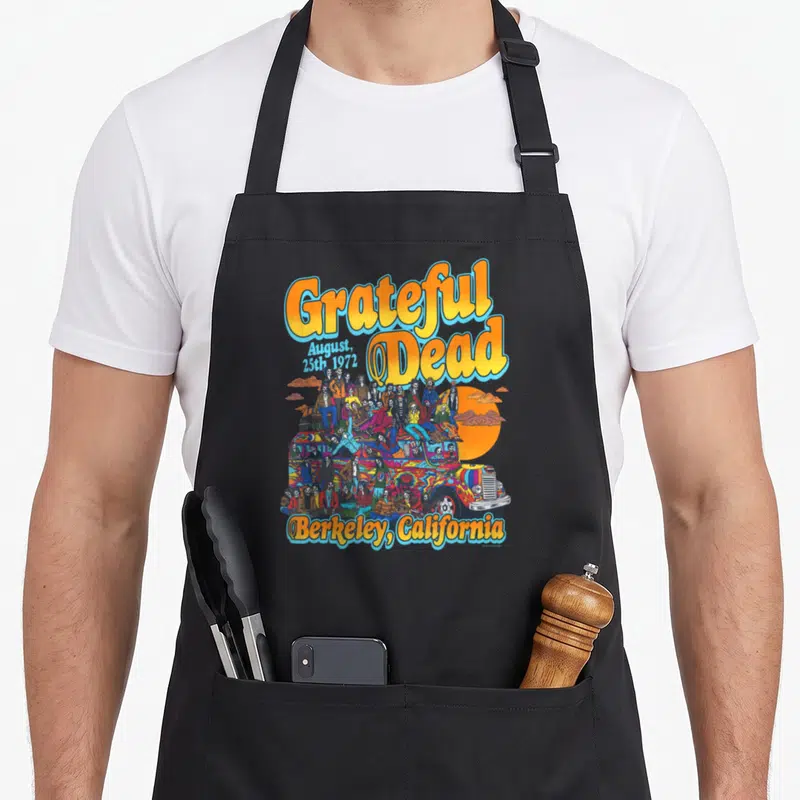 Berkeley grateful apron - Skeletons on colorful bus with Grateful Dead August 25th 1972 text — shown on a black cotton canvas apron against a white background