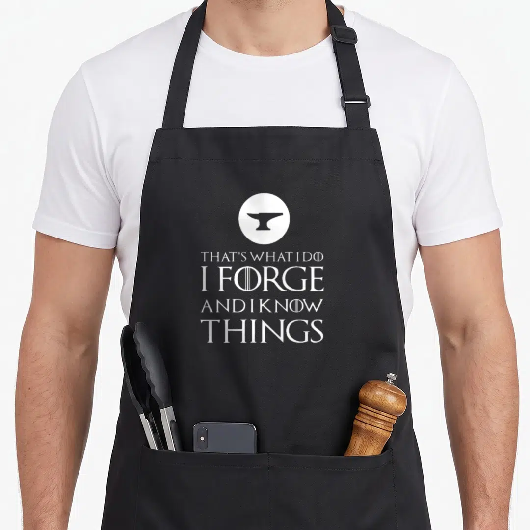 Forge blacksmith apron - White anvil in circle above stacked text reading THAT'S WHAT I DO I FORGE AND I KNOW THINGS — shown on a black cotton canvas apron against a white background