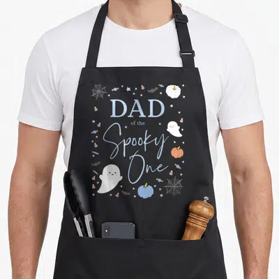 Birthday halloween apron - Dad of the Spooky One text with ghost, pumpkins, candy corn, and stars in blue white orange — shown on a black cotton canvas apron against a white background