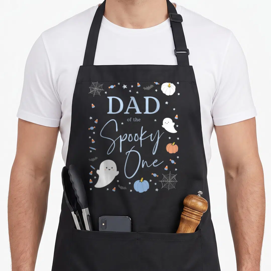 Birthday halloween apron - Dad of the Spooky One text with ghost, pumpkins, candy corn, and stars in blue white orange — shown on a black cotton canvas apron against a white background