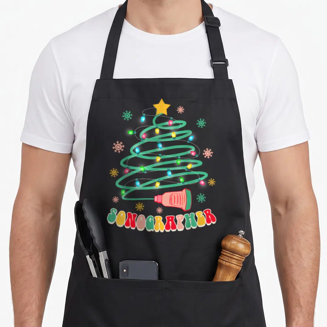 Sonographer christmas themed apron - Cartoon Christmas tree with colored bulbs, transducer, snowflakes, and arched — shown on a black cotton canvas apron against a white background