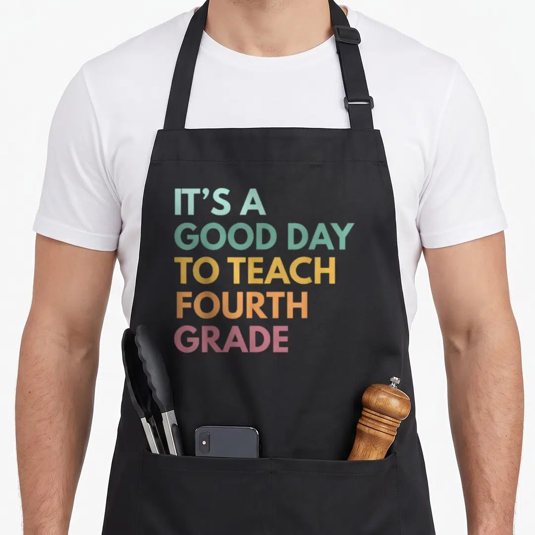 School teach fourth teacher apron - Stacked rainbow text reading IT'S A GOOD DAY TO TEACH FOURTH GRADE — shown on a black cotton canvas apron against a white background