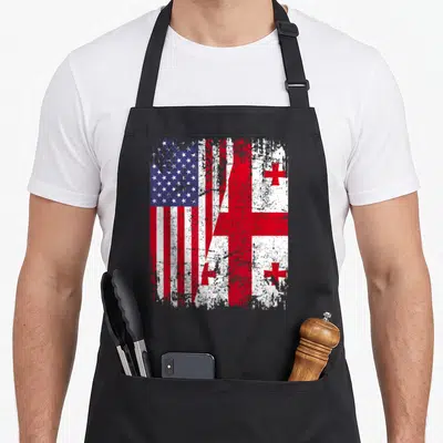 Georgian american flag apron - Two flags split diagonally in red white blue distressed texture — shown on a black cotton canvas apron against a white background