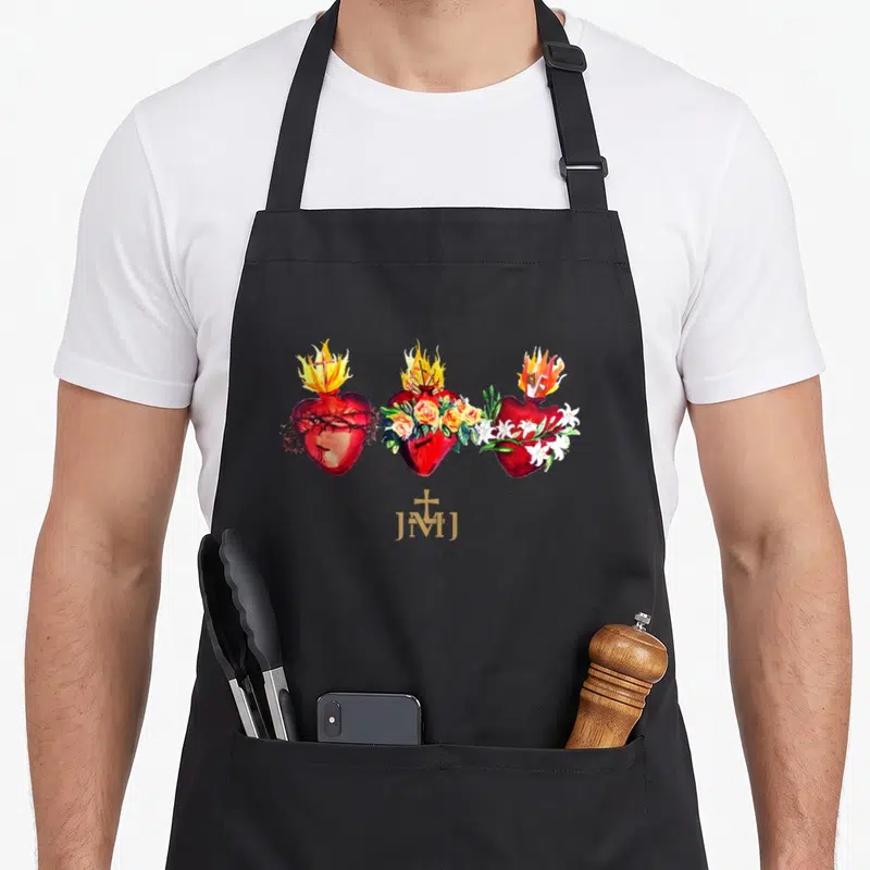 Three catholic apron - Three red hearts with thorns roses lilies and gold JMJ text in watercolor — shown on a black cotton canvas apron against a white background