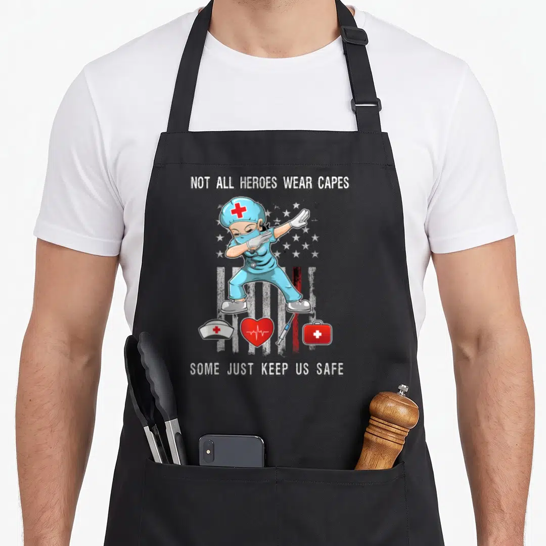 Cape nurse apron - Cartoon nurse in blue scrubs dabbing with medical icons and text about keeping us safe — shown on a black cotton canvas apron against a white background