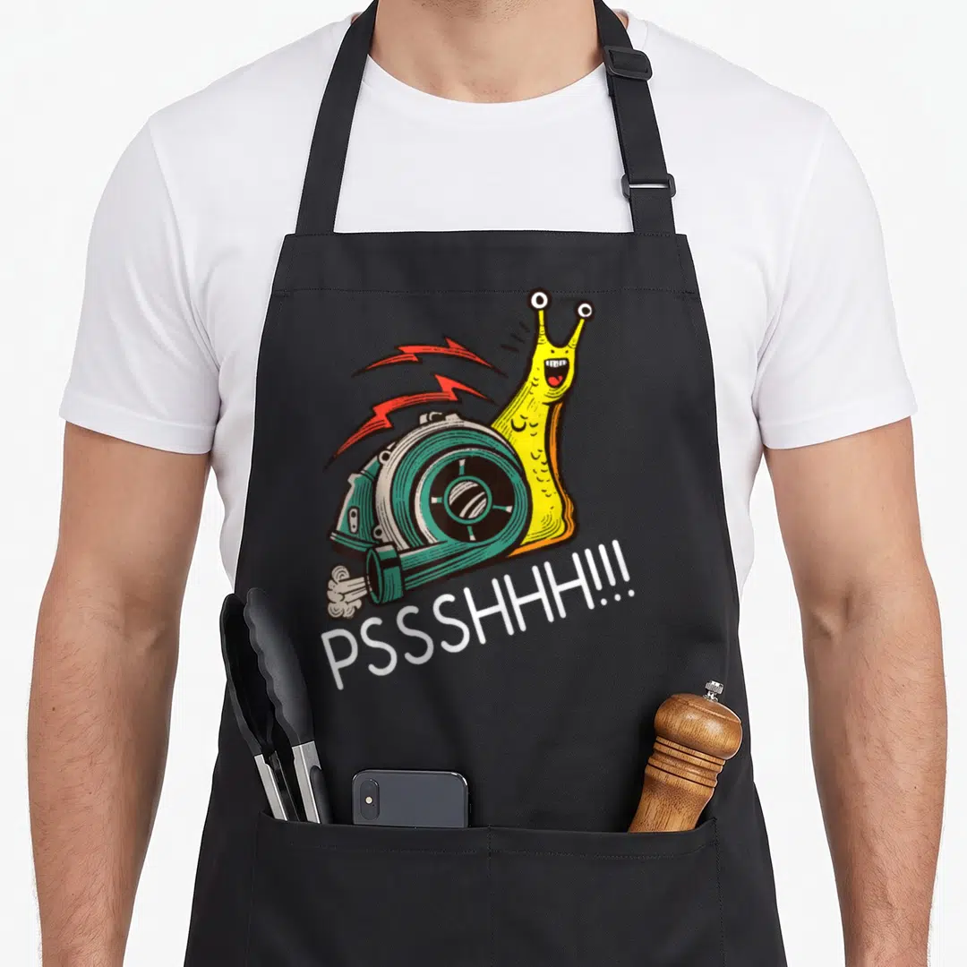Snail racing apron - Yellow snail with teal turbo shell and red lightning bolts above white PSSSHHH text — shown on a black cotton canvas apron against a white background
