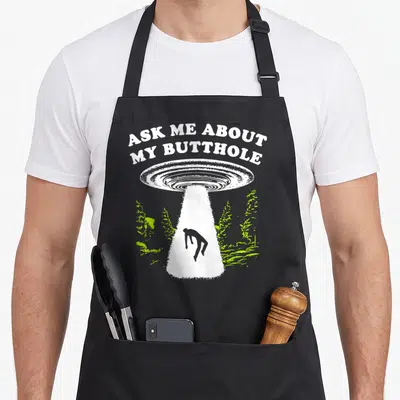 Butthole ask about apron - UFO beam lifting person under arched text ASK ME ABOUT MY BUTTHOLE with lime plants — shown on a black cotton canvas apron against a white background