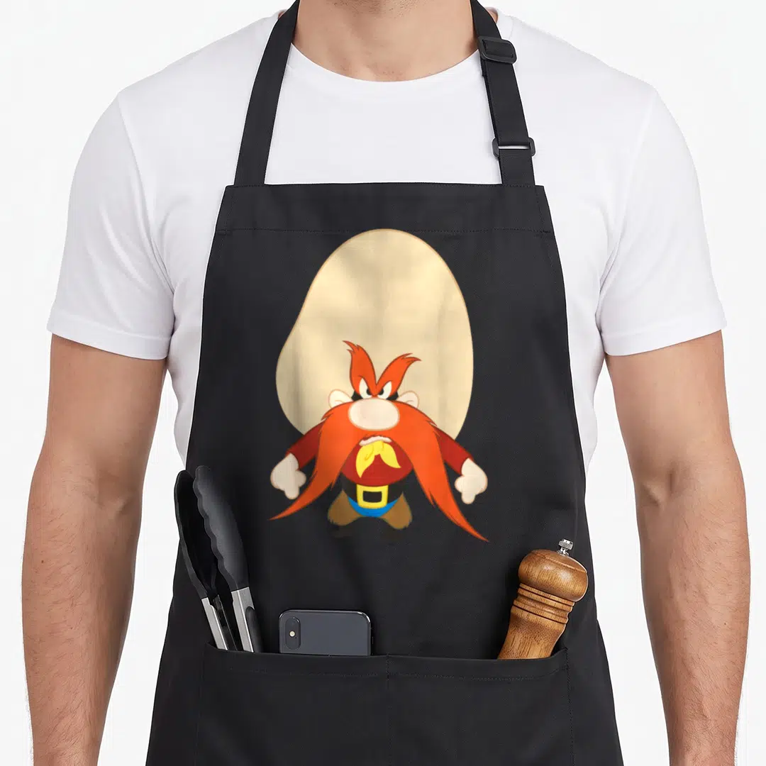 Yosemite looney tune apron - Angry cartoon character with orange beard standing before beige oval shape — shown on a black cotton canvas apron against a white background