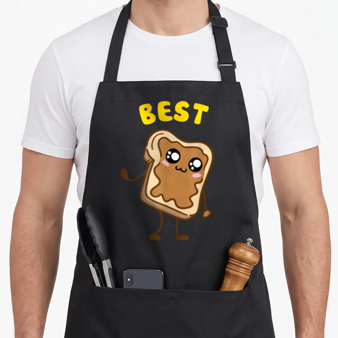 Bff butter apron - Cartoon toast with peanut butter, arms legs, BEST text above in yellow — shown on a black cotton canvas apron against a white background