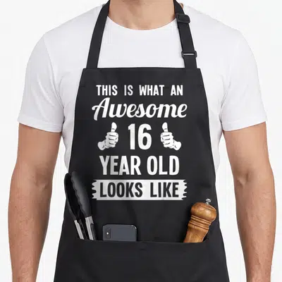Funny 16th birthday apron - Stacked white text reading THIS IS WHAT AN Awesome 16 YEAR OLD LOOKS LIKE flanked by thumbs — shown on a black cotton canvas apron against a white background