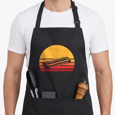 Harmonica french apron - Grey harmonica illustration over a retro sun with horizontal yellow, orange, and red stripes — shown on a black cotton canvas apron against a white background