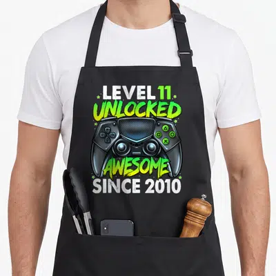 11th birthday gaming aprons - Game controller graphic with LEVEL 11 UNLOCKED AWESOME SINCE 2010 text in lime green — shown on a black cotton canvas apron against a white background