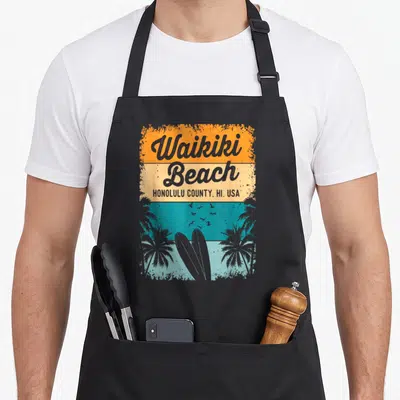 Waikiki honolulu apron - Retro Waikiki Beach text, two surfboards, palm trees, birds, striped orange beige teal blue — shown on a black cotton canvas apron against a white background