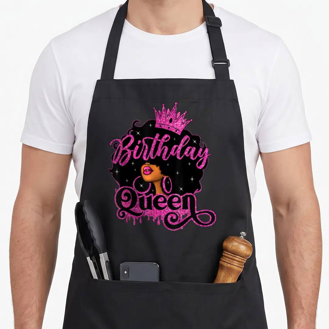Birthday african american aprons - Cartoon woman with Birthday Queen text, pink crown, sparkles in black hair — shown on a black cotton canvas apron against a white background