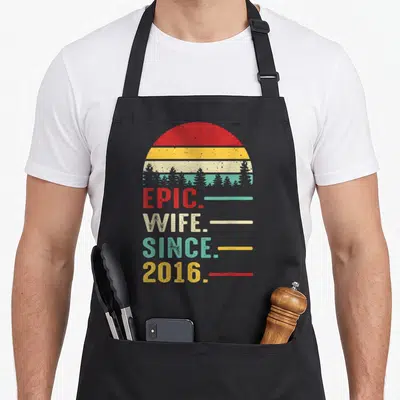 10th wedding apron - Retro sunset with tree silhouettes and stacked text reading epic wife since 2016 — shown on a black cotton canvas apron against a white background