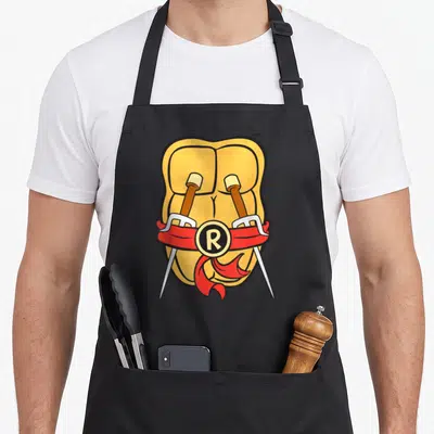Shell teenage cooking aprons - Cartoon muscular torso with crossed swords and red ribbon bearing R logo — shown on a black cotton canvas apron against a white background