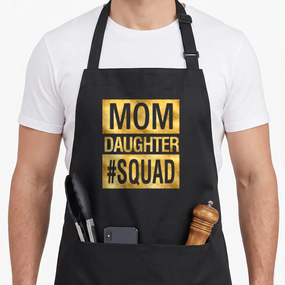 Squad mom daughter apron - MOM DAUGHTER #SQUAD text on gold rectangular backgrounds in grey font — shown on a black cotton canvas apron against a white background