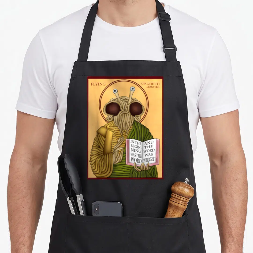 Monster flying apron - Cartoon FSM with halo holding book reading IN THE BEGINNING WAS THE WORD ARRRGEL — shown on a black cotton canvas apron against a white background