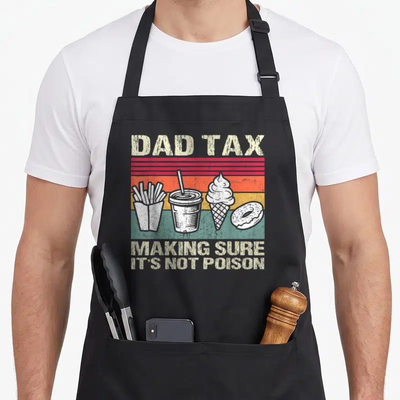 Father making an apron - Dad Tax text above four white fast food items on red orange yellow stripes — shown on a black cotton canvas apron against a white background