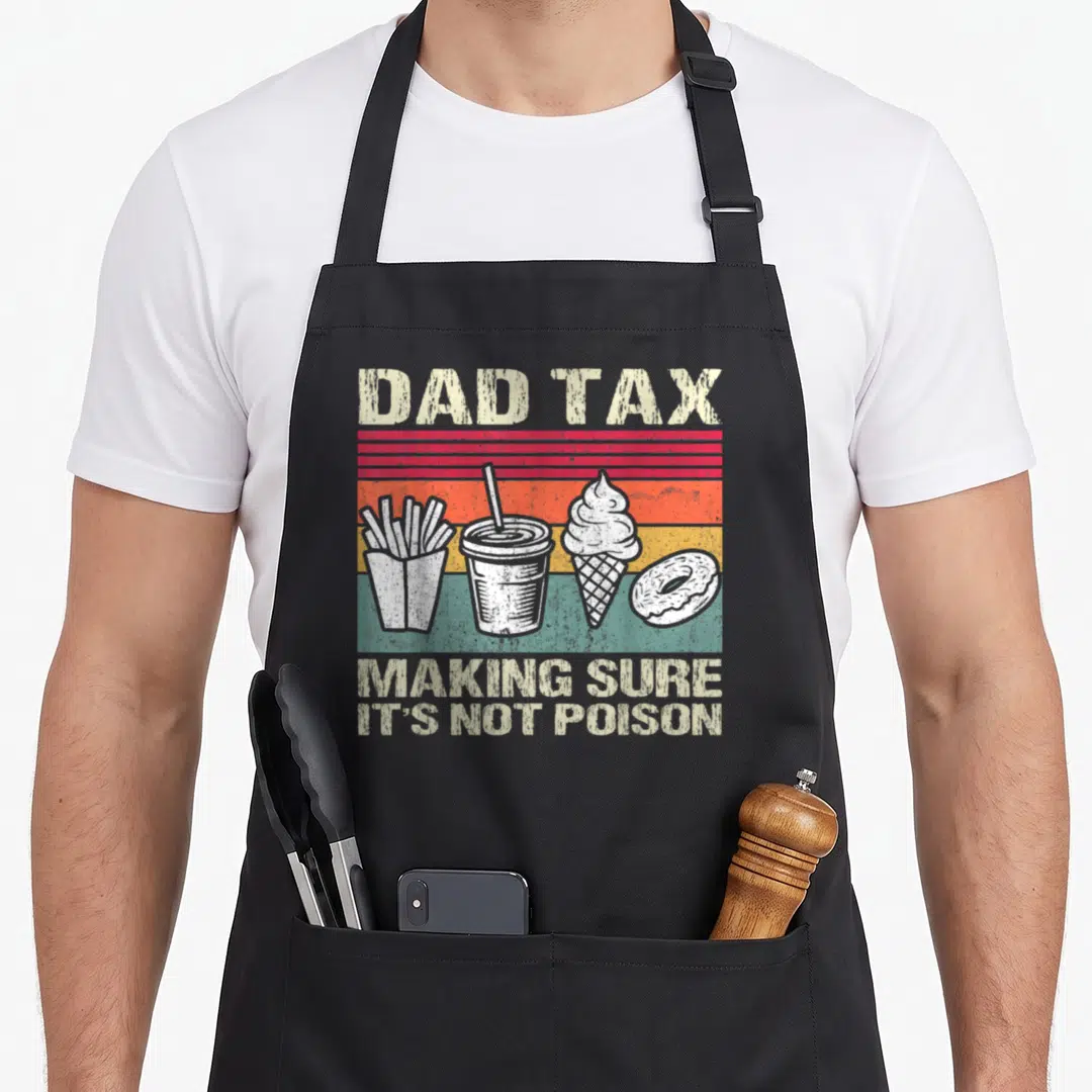 Father making an apron - Dad Tax text above four white fast food items on red orange yellow stripes — shown on a black cotton canvas apron against a white background