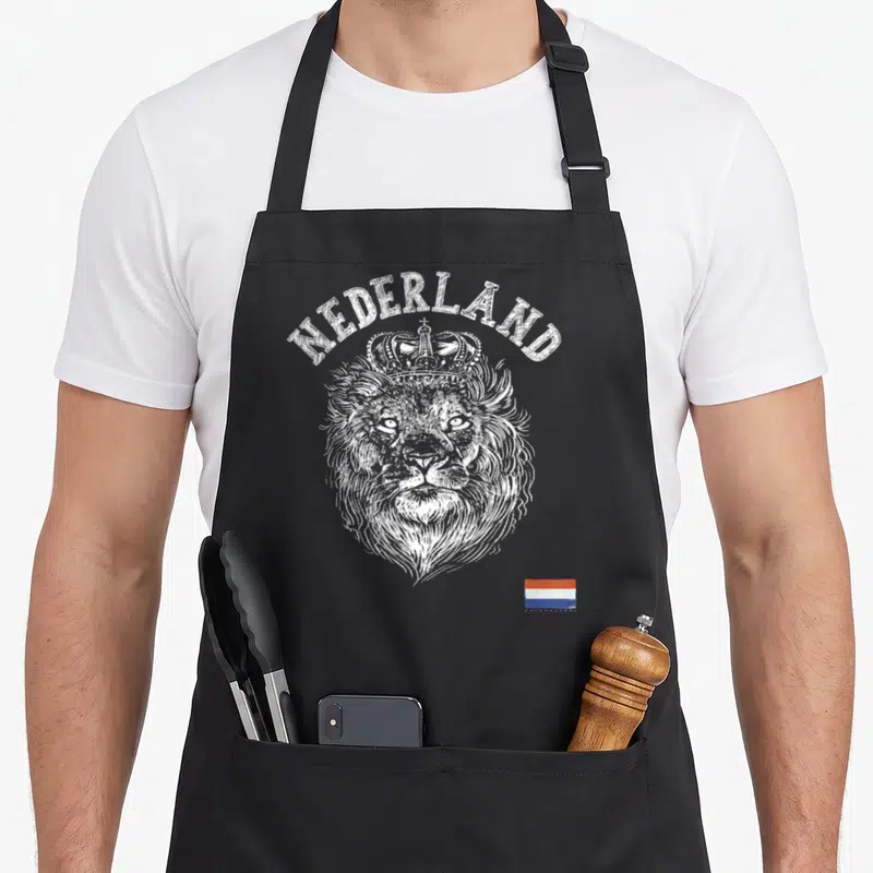 Nederland dutch apron - Crowned lion head with NEDERLAND text and red white blue flag in white line art — shown on a black cotton canvas apron against a white background