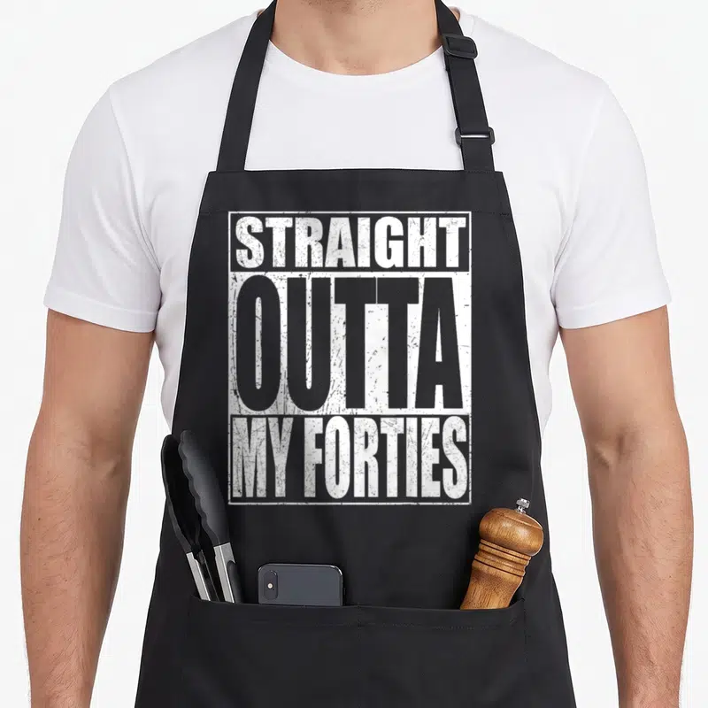 Outta forty birthday apron - Stacked white and grey text reading straight outta my forties inside a rectangular border — shown on a black cotton canvas apron against a white background