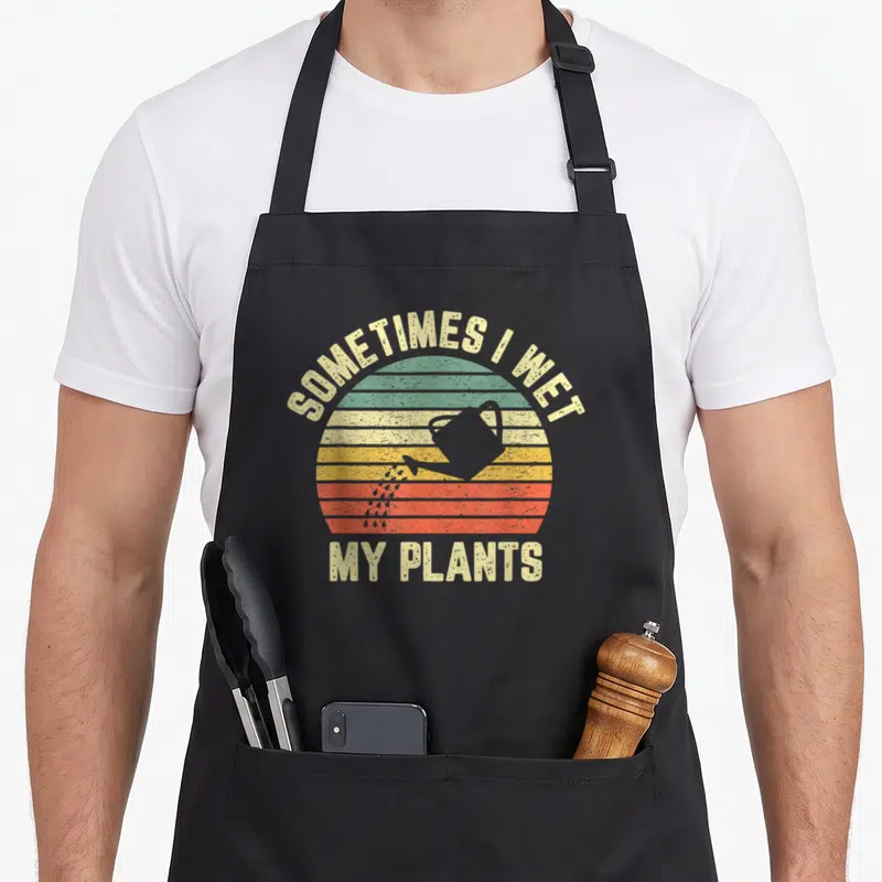 Gardening plant apron - Retro striped sun with watering can and SOMETIMES I WET MY PLANTS text — shown on a black cotton canvas apron against a white background